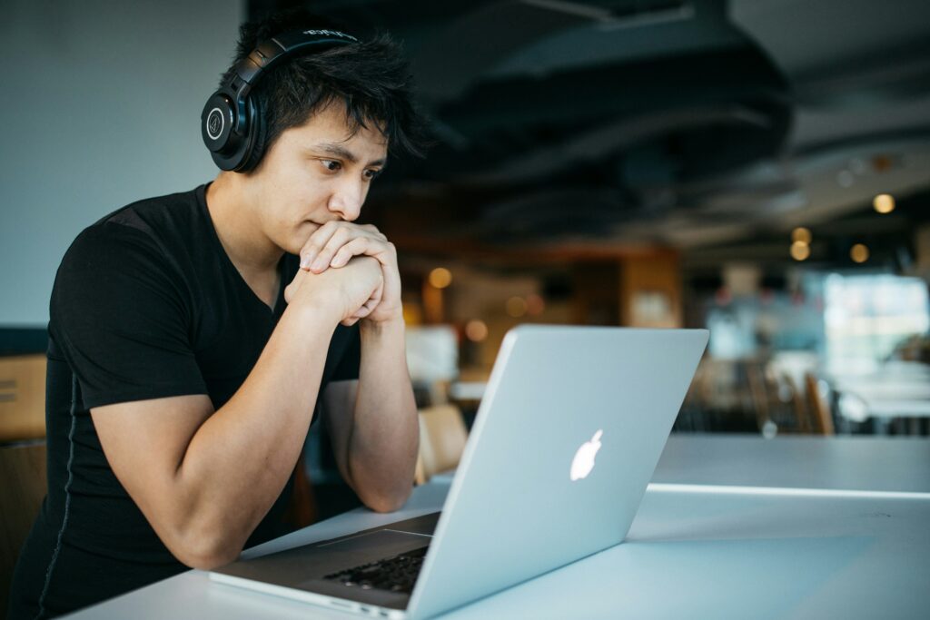 Um jovem usando fones de ouvido enquanto participa de uma terapia online em seu laptop. O cenário moderno e casual sugere um ambiente flexível, ideal para sessões de psicanálise online.